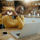 Happy black woman showing heart shape to someone during video ca
